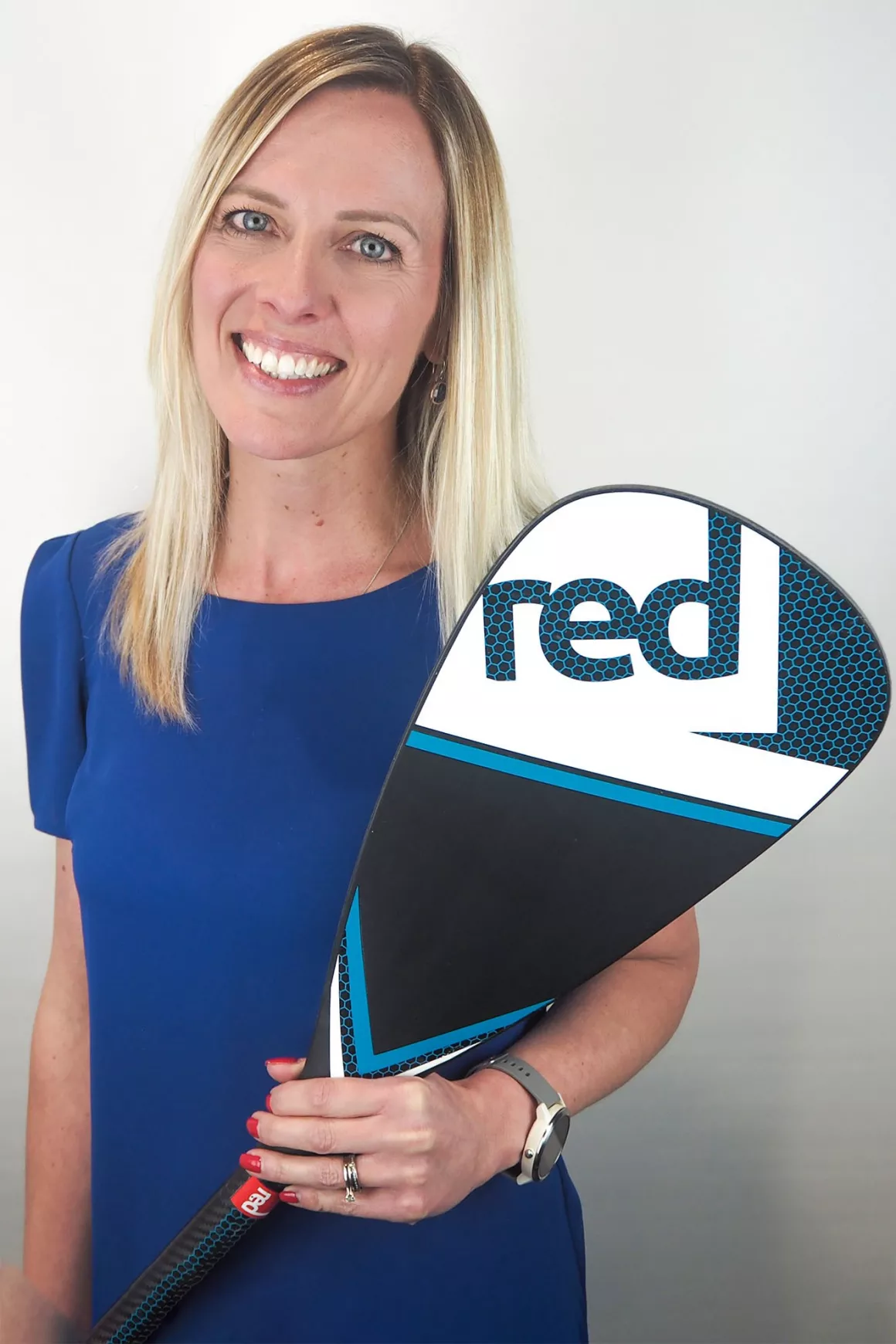 Layla Drewell (Finance Director) wearing a blue dress holding a paddle board awe, photo taken at Prime Appointments HQ