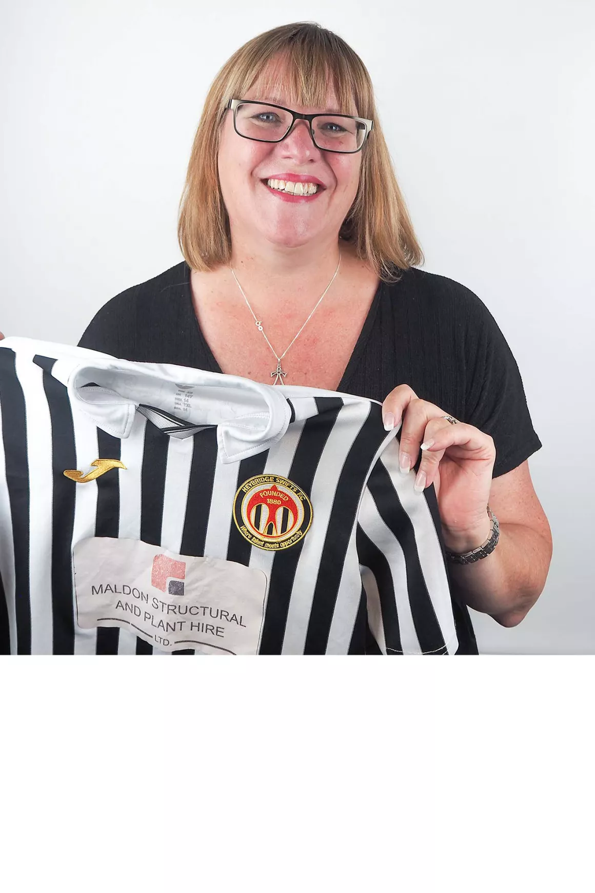 Nicola Edmead wearing black top and black glasses, holding prop which is a football shirt