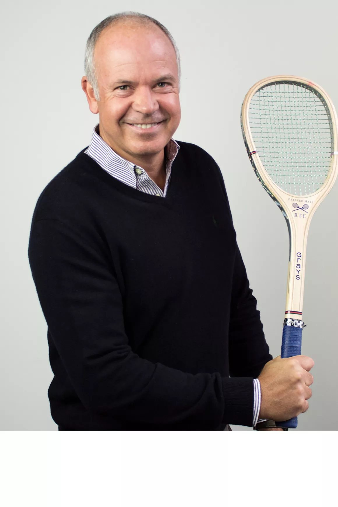 Peter Holmes (Director) wearing blue shirt and black jumper, holding real tennis racquet, photo taken at Prime Appointments HQ