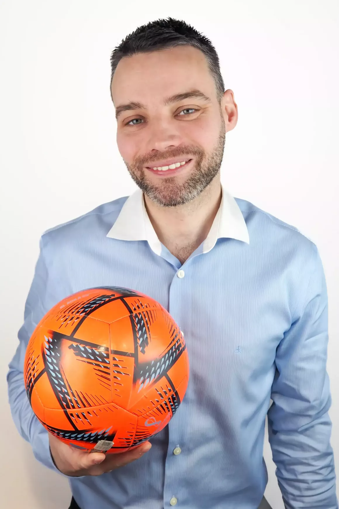Mitchell Burne (Consultant) Wearing a blue shirt and holding a prop (orange football), photo taken with white background